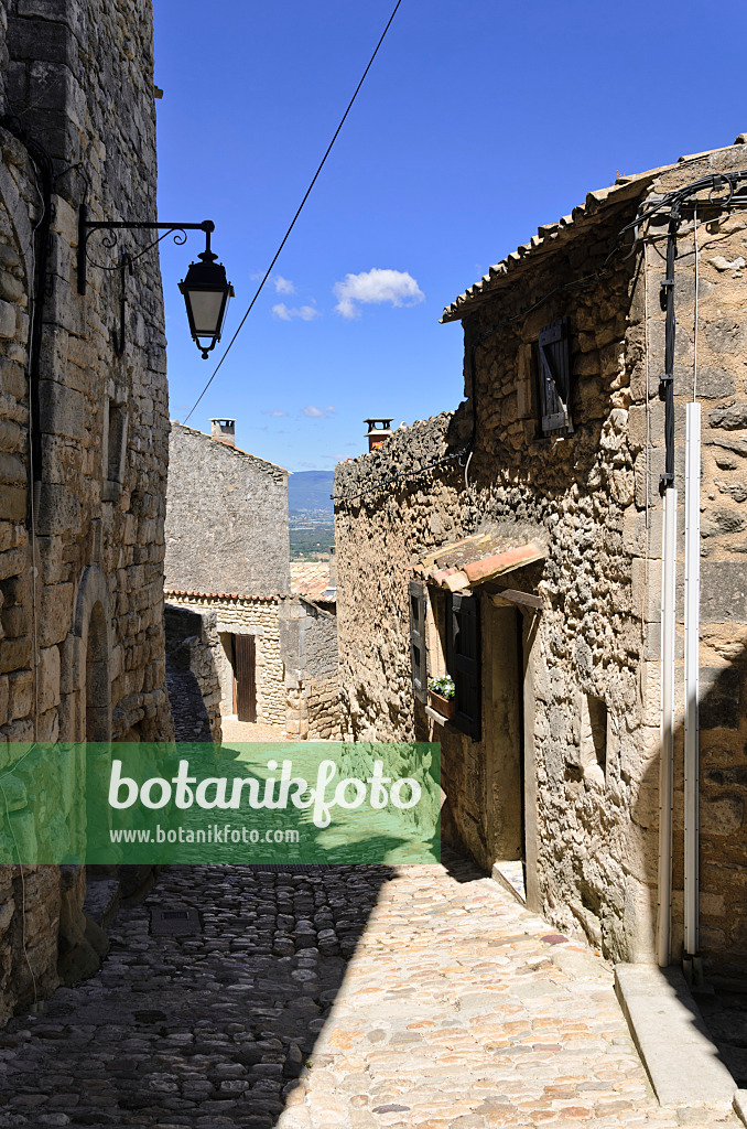 557162 - Gepflasterter Weg zwischen Häusern mit Feldsteinmauern und eiserner Laterne, Lacoste, Provence, Frankreich