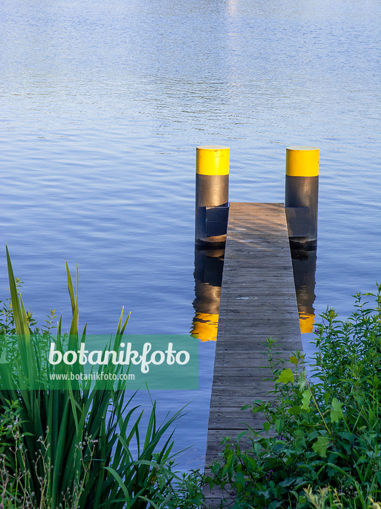 451018 - Schmaler Bootssteg aus Holzlatten mit zwei schwarzgelb bemalten Pontons in blauem Wasser