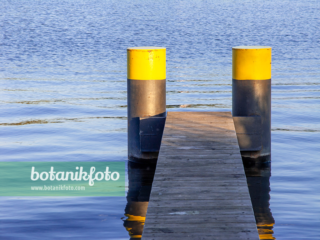 451019 - Schmaler Bootssteg aus Holzlatten mit zwei schwarzgelb bemalten Pontons in blauem Wasser