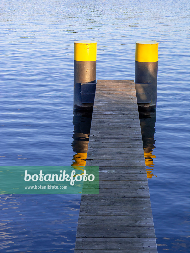 451020 - Schmaler Bootssteg aus Holzlatten mit zwei schwarzgelb bemalten Pontons in blauem Wasser