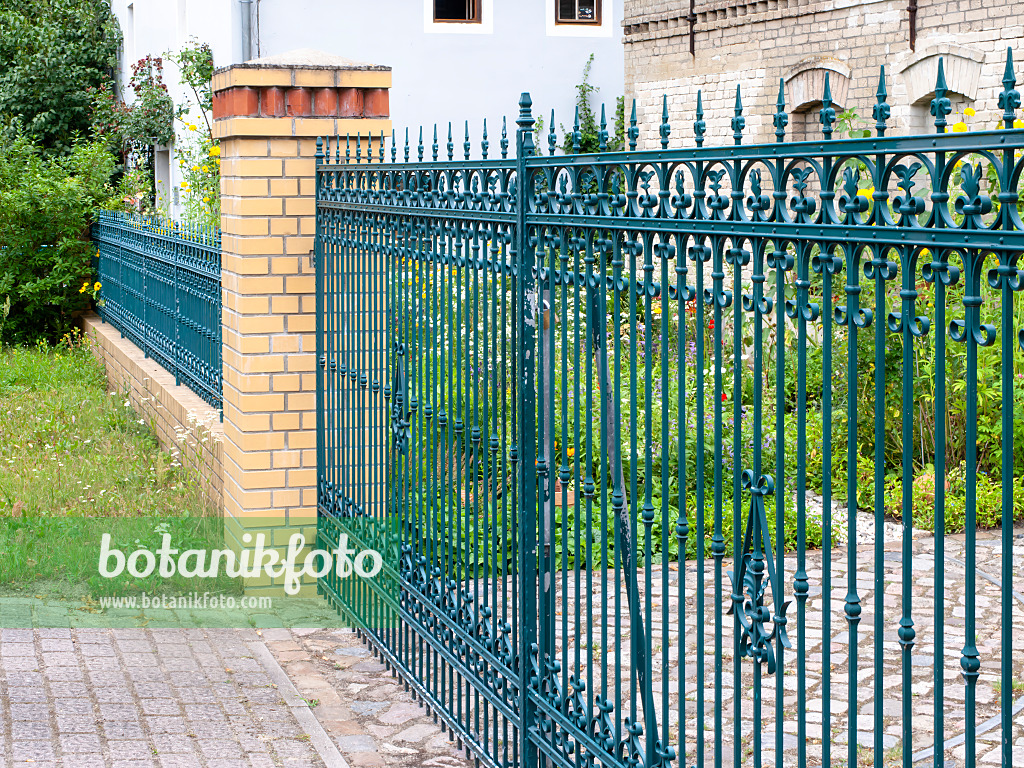 474285 - Blue cast-iron garden fence with brick platforms in front of a blooming front garden of an old farmstead