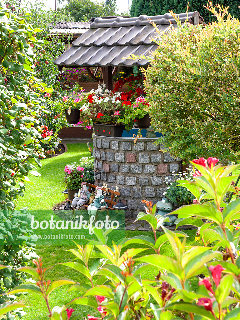 476181 - Round draw well with paving stones and a roof with shingles in a flowering garden