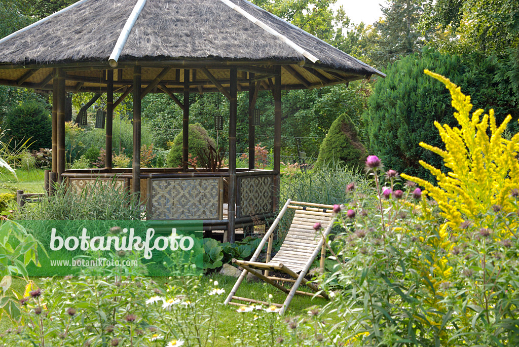 463077 - Round garden pavilion with wooden deck chair in a flowering garden