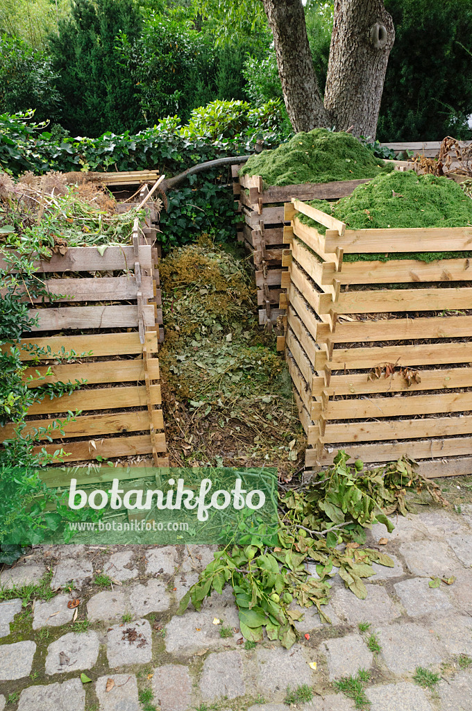 474075 - Composteur en bois avec des déchets de jardin et des tontes de pelouse fraîches sur une surface pavée dans le jardin