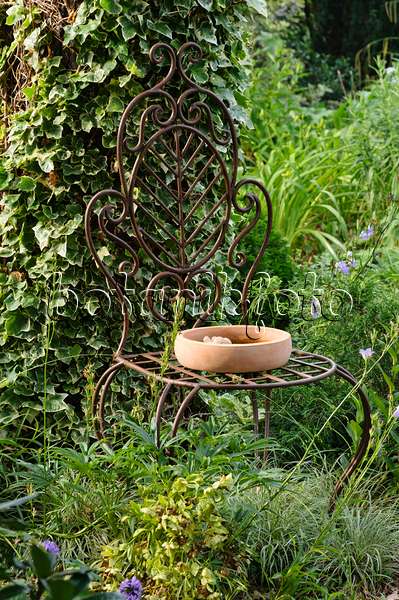 486035 - Alter, geschwungener Stuhl mit Rocaillen aus Gusseisen mit einer runden Vogeltränke aus Ton in einem Garten