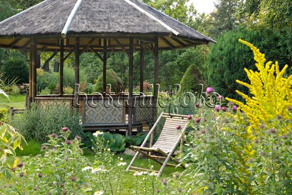463077 - Runder Gartenpavillon mit Liegestuhl aus Holz in einem blühenden Garten
