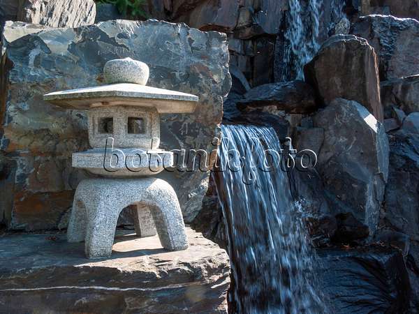 417014 - Asian stone lantern standing on a stone block in front of a waterfall with large granite blocks