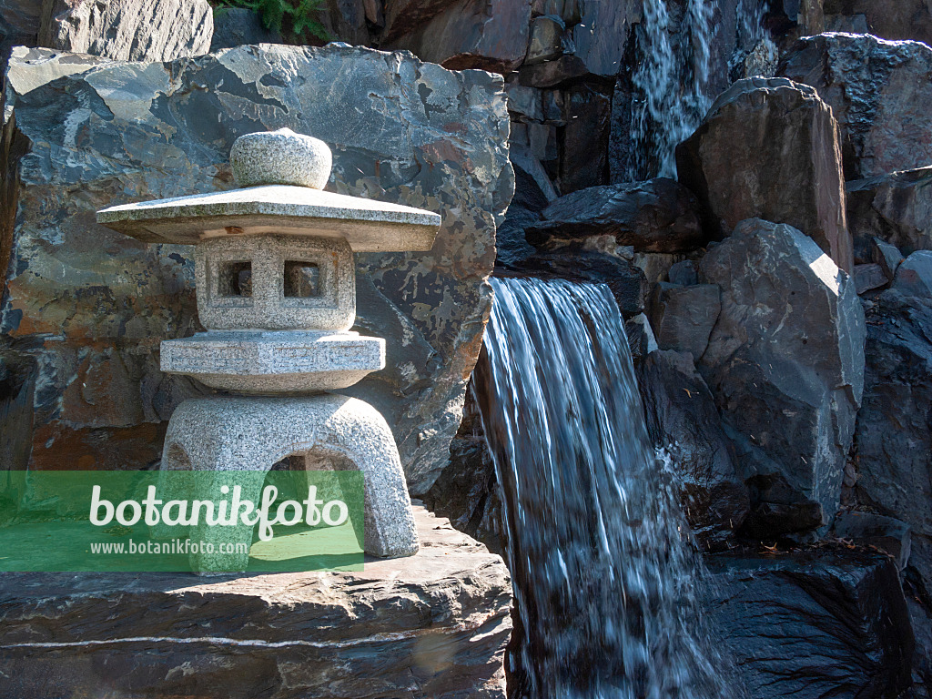 417014 - Asian stone lantern standing on a stone block in front of a waterfall with large granite blocks