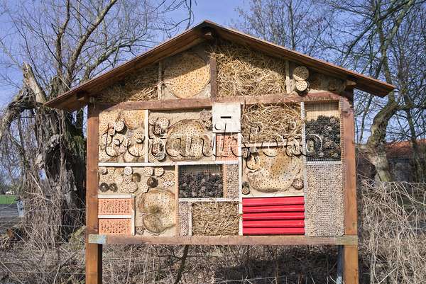 566083 - Large insect hotel with a gabled roof and perforated trunks, branches and bricks, pine cones and straw