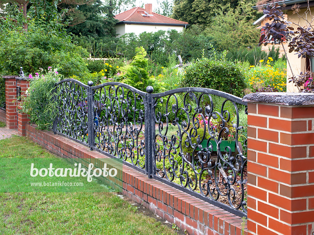 474422 - Curved metal fence on a brick wall in front of a flowering front garden