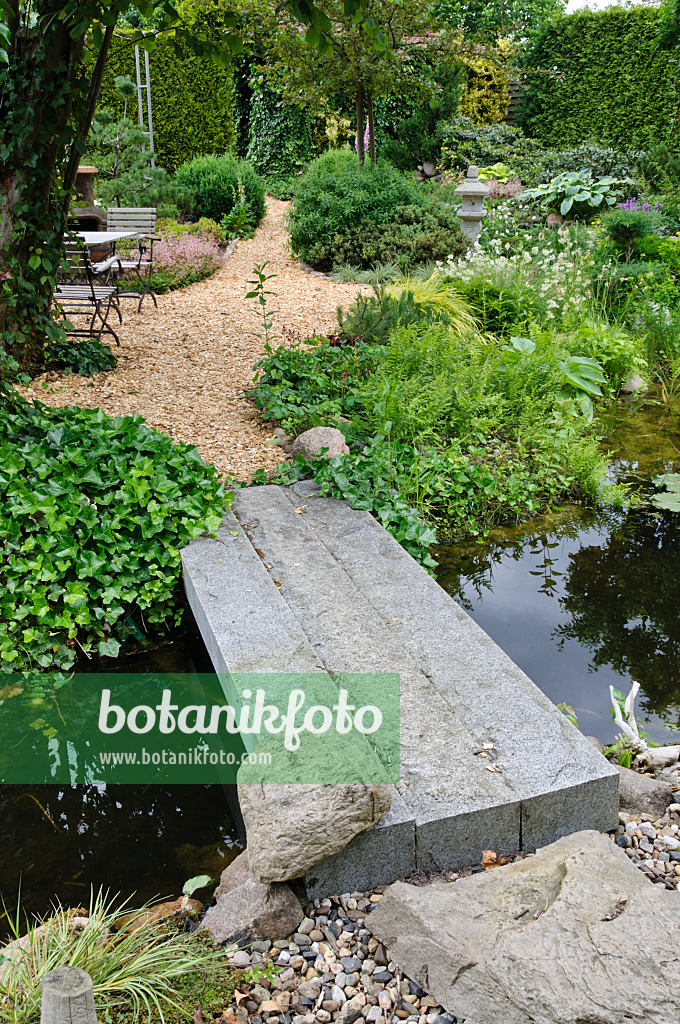 473082 - Garden pond with stone bridge and seating for relaxing in a well-kept park