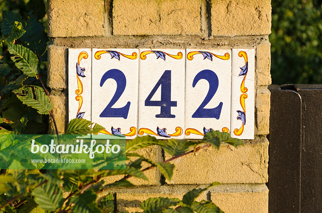 477172 - Number plate made of painted wall tiles on a brick wall in front of a garden