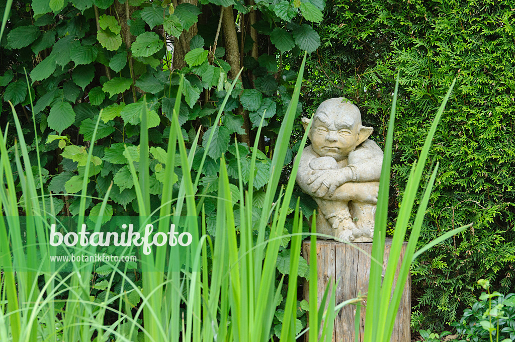 473116 - Sculpture of a gnome or gargoyle of stone on a wooden peg in a garden