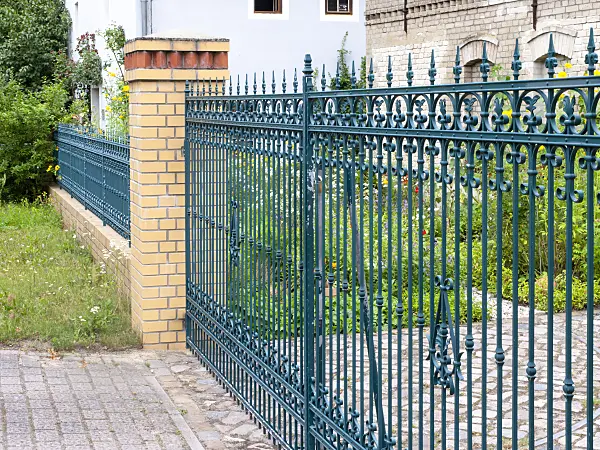 474285 - Blue cast-iron garden fence with brick platforms in front of a blooming front garden of an old farmstead