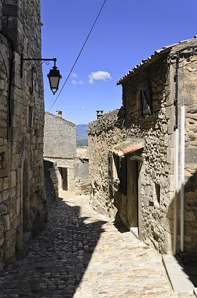 557162 - Cobbled path between houses with stone walls and iron lantern, Lacoste, Provence, France