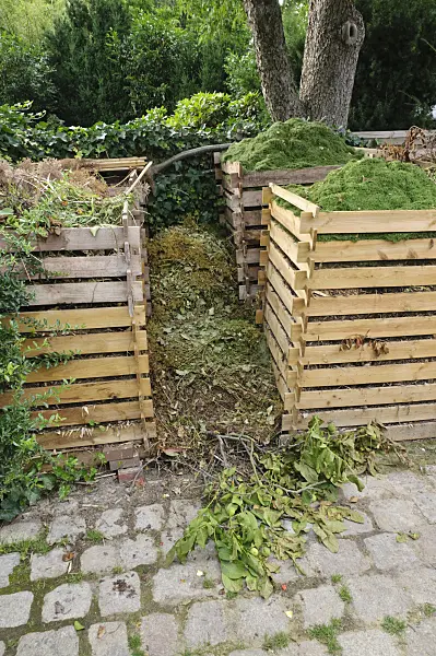 474075 - Composter made of wood with garden waste and fresh lawn mowing on a paved square in the garden