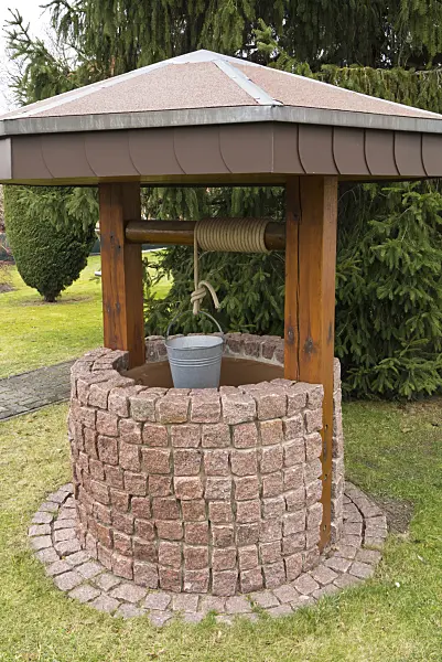 541004 - Draw well made of stone blocks with bucket hanging from a rope in a garden