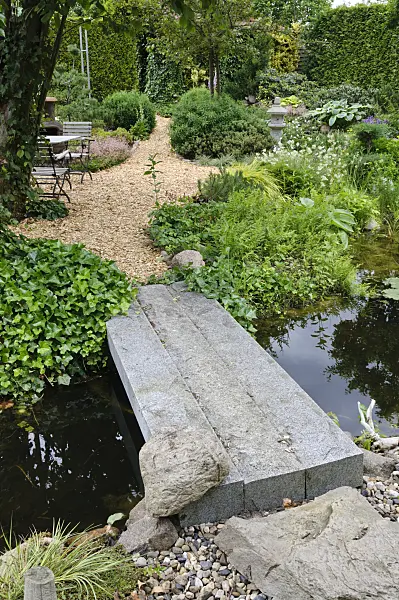 473082 - Garden pond with stone bridge and seating for relaxing in a well-kept park