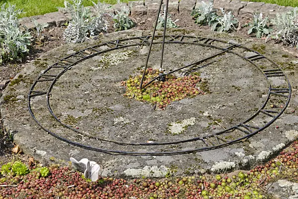 509149 - Metal sundial on a stone slab in the bed of a garden