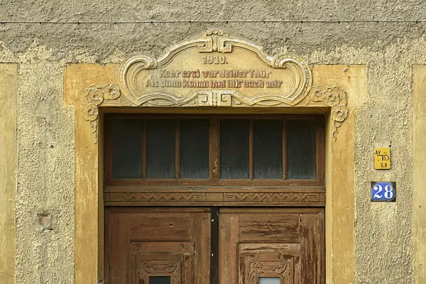 559034 - Old house entrance with double wooden door and saying of wisdom on a stone cornice, Görlitz, Germany