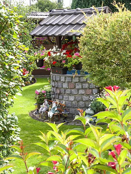 476181 - Round draw well with paving stones and a roof with shingles in a flowering garden