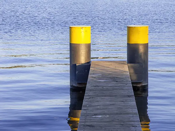 451019 - Schmaler Bootssteg aus Holzlatten mit zwei schwarzgelb bemalten Pontons in blauem Wasser