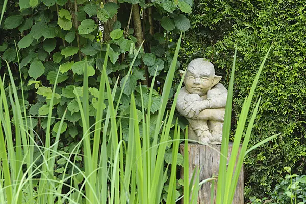 473116 - Sculpture of a gnome or gargoyle of stone on a wooden peg in a garden