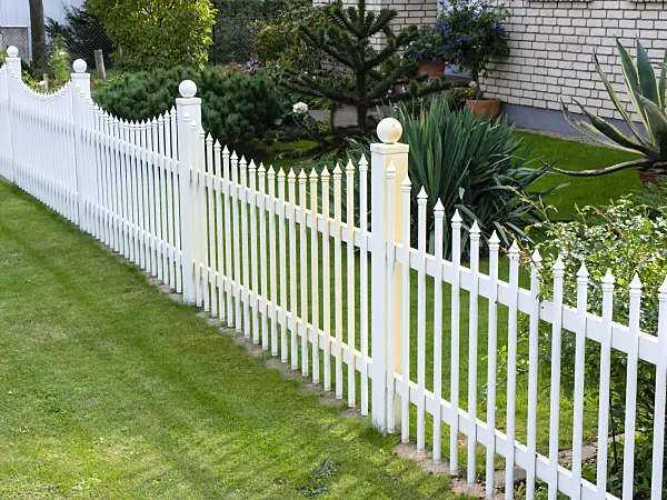 476187 - White palisade fence with curved arches in front of a front garden with tropical vegetation